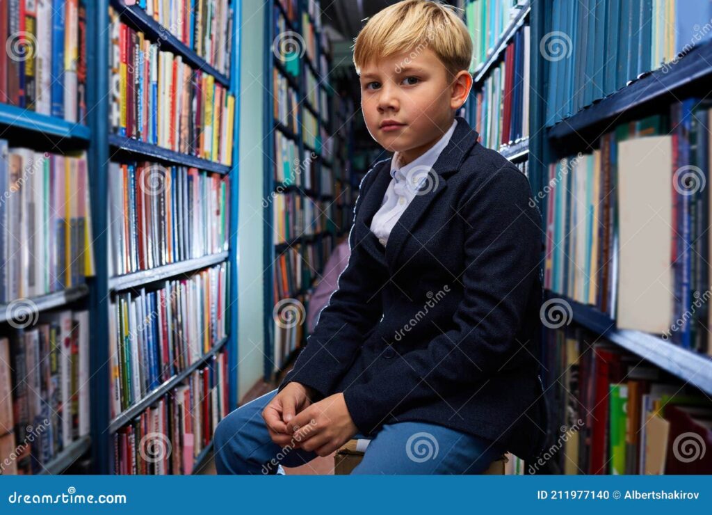 retrato de nino erudito sentado entre libros en biblioteca chico estantes busca del libro mas interesante mira camara serio 211977140