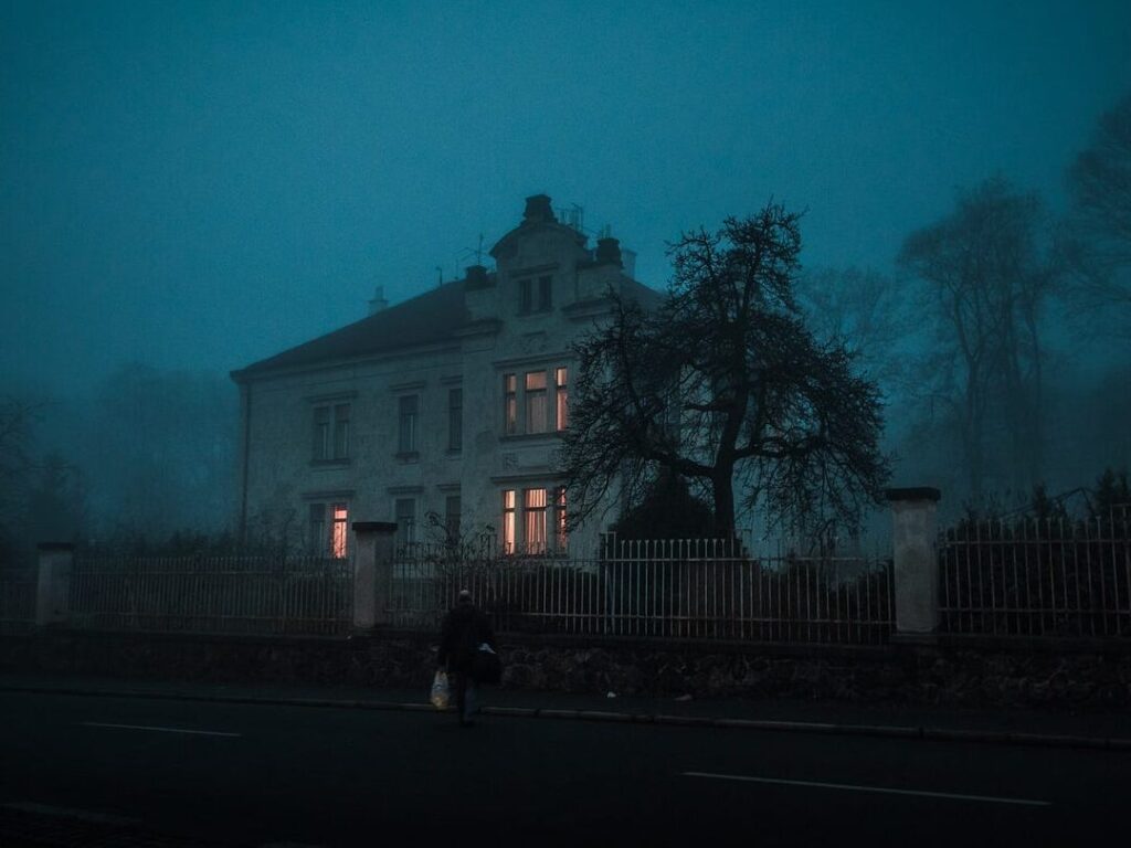 una imagen de una casa antigua y oscura rodeada de niebla con ventanas rotas y una puerta entreabierta