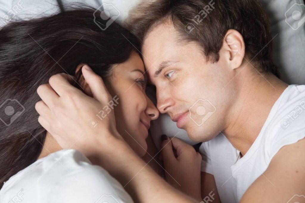 una imagen de una pareja acurrucada en la cama con una luz suave y una sonrisa relajada en el rostro de la mujer