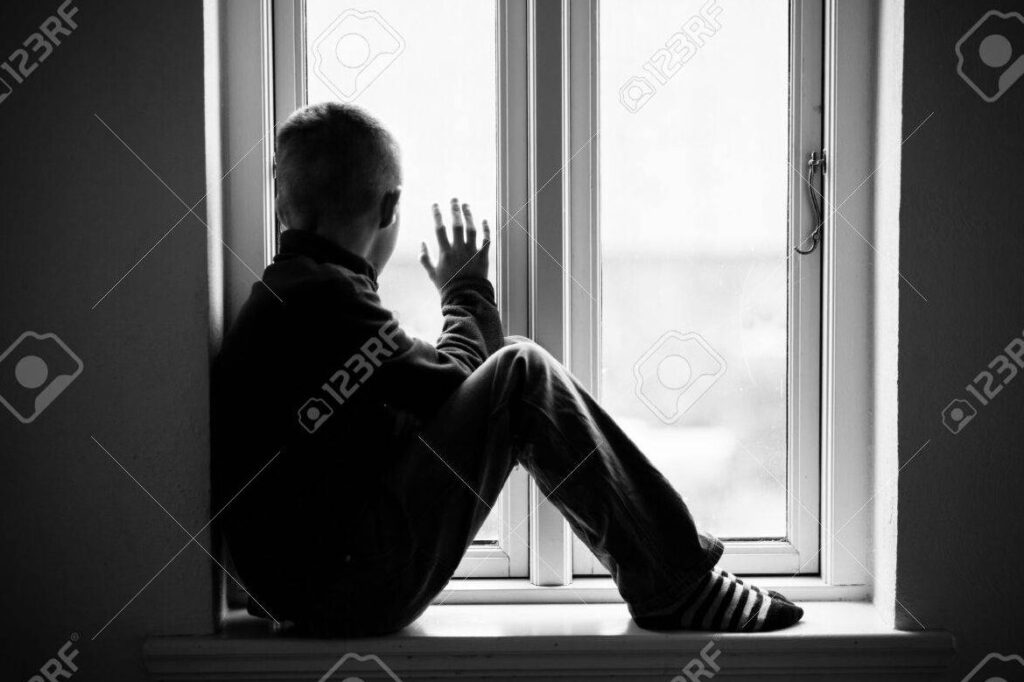 una imagen en blanco y negro de una persona solitaria mirando por la ventana con expresion triste