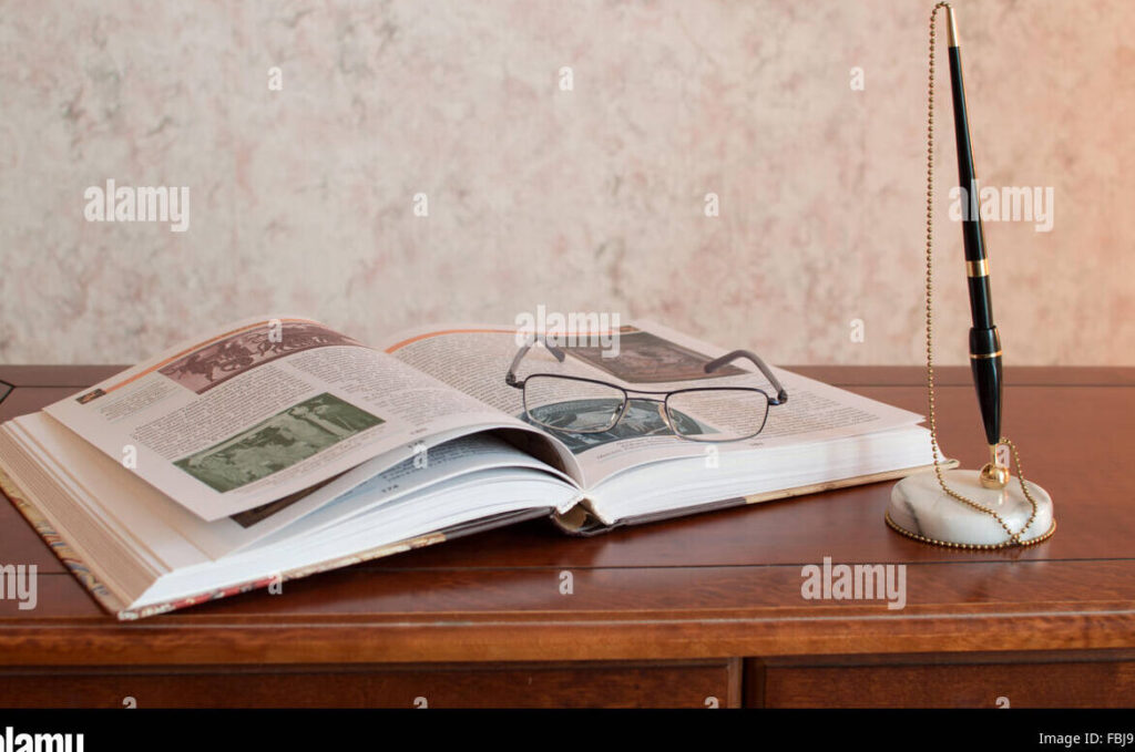 una imagen que represente una mesa de escritorio con una pluma un cuaderno y algunos libros abiertos
