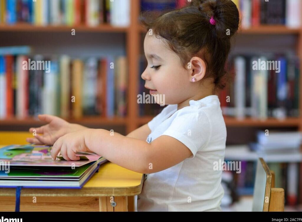 una nina sonriente leyendo un libro rodeada de estantes llenos de libros coloridos