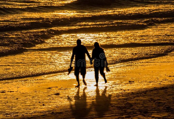 una pareja caminando de la mano al atardecer en la playa