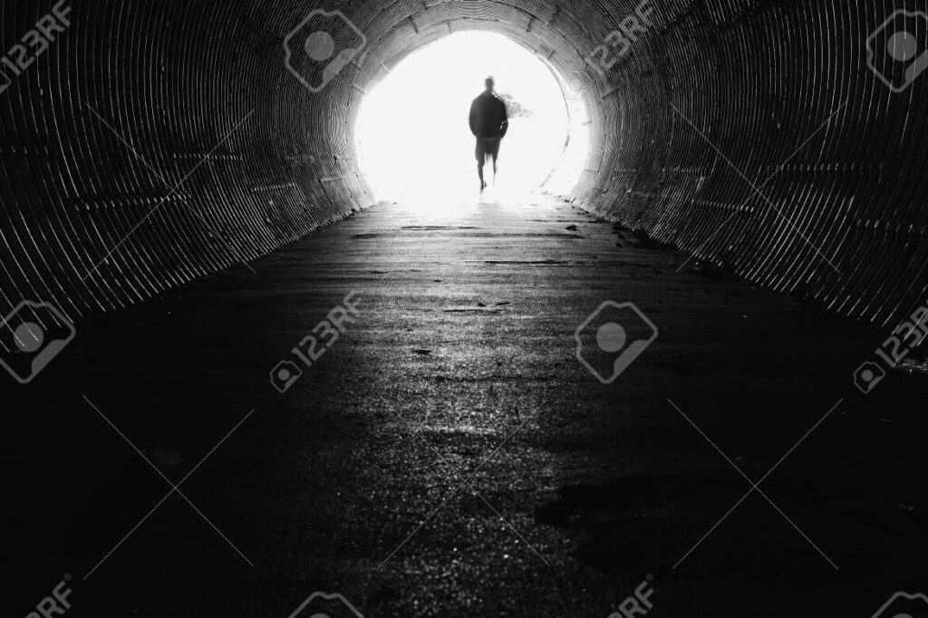 una persona caminando hacia la luz al final de un tunel oscuro